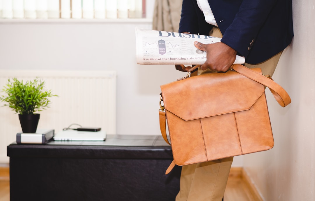 Business professional carrying a leather briefcase and financial newspaper in an office